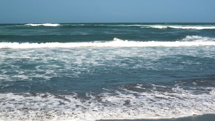 Waves crashing against the shore with a clear blue sky in the background at Parangtritis Beach, Yogyakarta.