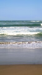Waves crashing against the shore with a clear blue sky in the background at Parangtritis Beach, Yogyakarta.