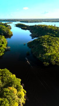Vertical: Drone follows boat down Juma River with lush trees on both sides in Amazon Jungle, Brazil