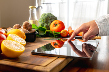 A woman is looking for a recipe on a tablet while preparing fresh vegetables on a wooden cutting board, healthy food concept
