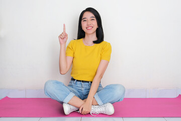 A woman sitting cross legged and pointing up with happy expression
