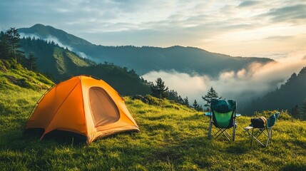 Scenic campsite featuring a tent, portable chairs, and a backpack on green grass, surrounded by misty mountains.