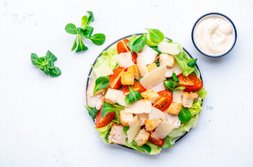 Delicious salad with chicken, tomatoes, iceberg salad, croutons, parmesan cheese and caesar dressing. White background, top view