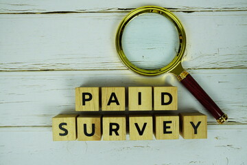 Paid Survey with wooden blocks alphabet letters and magnifying glass top view on wooden background