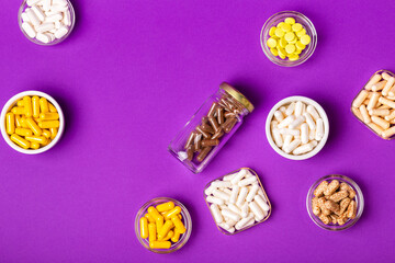 Organic dietary supplements, many capsules of vitamins and minerals in small bowls from above on violet background. Nutritional supplements, pills and tablets, top view. Healthy lifestyle.