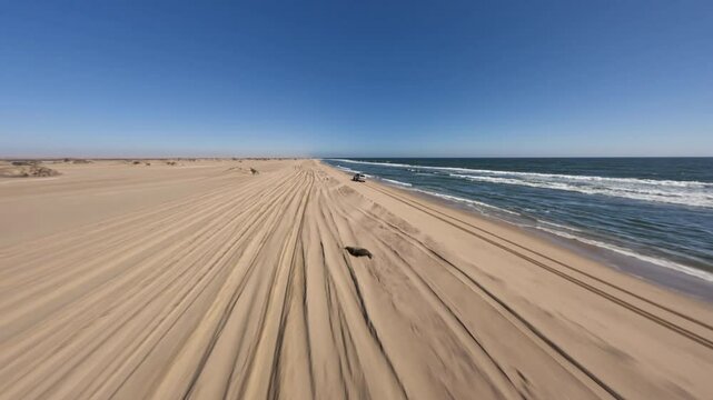 Aerial view with FPV drone of a 4x4 driving along the beaches on the edge of the ocean next to the Namib dunes on a beautiful day of adventure at sunset, Namibia, Africa