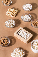 Organic dietary supplements, many capsules of vitamins and minerals in small bowls from above on kraft background. Nutritional supplements, pills and tablets, top view. Healthy lifestyle.