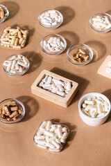 Organic dietary supplements, many capsules of vitamins and minerals in small bowls from above on kraft background. Nutritional supplements, pills and tablets, top view. Healthy lifestyle.