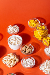 Organic dietary supplements, many capsules of vitamins and minerals in small bowls from above on an orange background. Nutritional supplements, pills and tablets, top view. Healthy lifestyle.