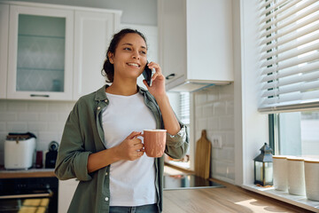 Smiling Latin woman talking on mobile phone while having  cup of coffee.