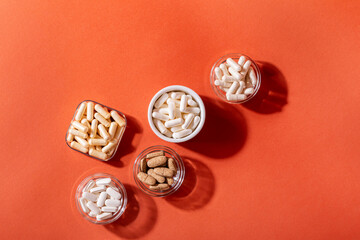 Organic dietary supplements, many capsules of vitamins and minerals in small bowls from above on an orange background. Nutritional supplements, pills and tablets, top view. Healthy lifestyle.