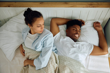 Restless woman looking at her boyfriend who is sleeping carelessly beside her.
