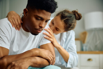 Sad black man being consoled by his girlfriend in bedroom.