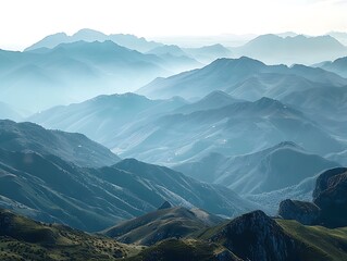 A majestic mountain range viewed from a high vantage point with rolling hills and valleys stretching out below The distant peaks are shrouded in mist adding a touch of mystery to the landscape