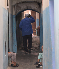 Narrow street in the Medina of Tetouan, T&eacute;touan, Morocco. Man walking. Legs of two girls sitting.