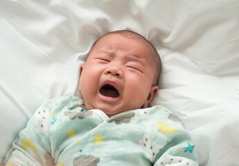 Asian newborn baby lying on his back in bed and cry from hunger, baby screams loudly.