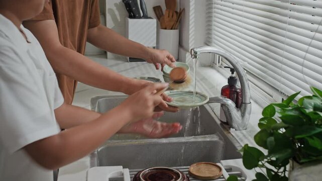 Cropped shot of teenage boy and his dad cleaning dishes after meal in kitchen sink