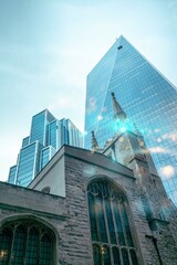 An old stone church building with a large arched window stands against a backdrop of modern glass...