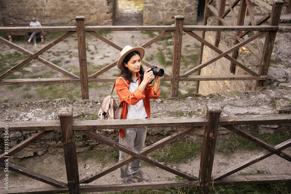 Wall mural female traveler carefully takes photos while exploring ancient fortress. holding her camera