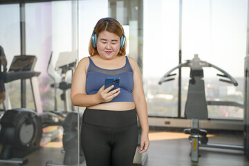 Obese asian woman Enjoy listening to music. Fat Female with headphones smart phone after workout at Gym