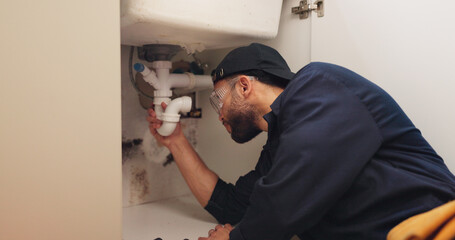 Plumber, man and pipeline installation in kitchen with safety for home maintenance or fixing leak by sink. Plumbing contractor, handyman or working on filter system repair for small business in house