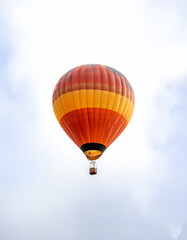 Fototapeta premium A vibrant orange and yellow hot air balloon ascends against a clear white sky.