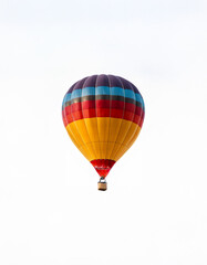 Fototapeta premium A colorful hot air balloon with a wicker basket rises against a white sky.