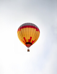 Fototapeta premium A red, yellow, and gray hot air balloon floats against a white sky.