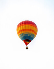 Naklejka premium A colorful hot air balloon with a wicker basket floats against a white sky.