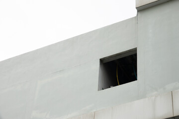 A window is visible in the middle of a white wall. The window is small and has a yellow wire coming out of it. The wall is very plain and has no decorations