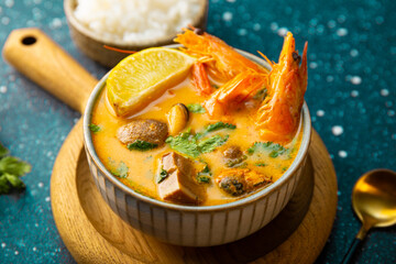 A bowl of tom yum soup with shrimp, sea food and lime close up