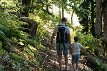 man and child trekking in forest descending from slope. Father supporting son holding him by hand