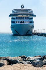 A large cruise ship is docked at a port, with the bow of the ship facing the camera. The water is...