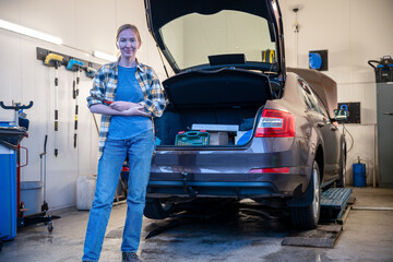 female mechanic holding work tool and standing at entrance of garage