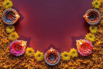 Decorative clay diya lamps for Diwali festival with Chrysanthemum flowers puts and orange marigold petals on red background.