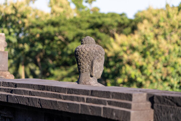 Buddha statue from the back, in front of stone relief wall at the ancient historical Buddhist UNESCO site of Borobudur (Barabudur), Magelang, Indonesia.