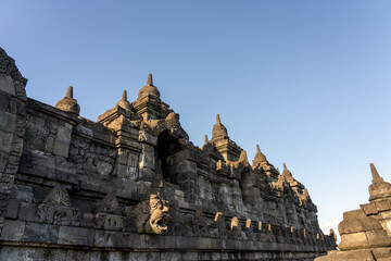 Sunset light on ancient reliefs, stupa and Buddha statues in niche with moon in background between stupas, at the ancient historical Buddhist UNESCO site of Borobudur (Barabudur), Magelang, Indonesia.