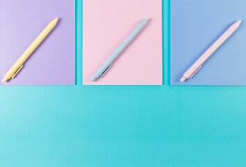 Top view of pink, purple and blue notebooks on blue background. Pink, yellow and blue pens, school, office wallpaper. Flat lay, copy space.