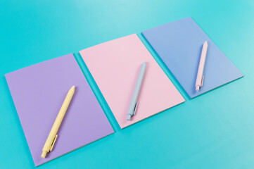 Top view of pink, purple and blue notebooks on blue background. Pink, yellow and blue pens, school, office wallpaper. Flat lay, copy space.