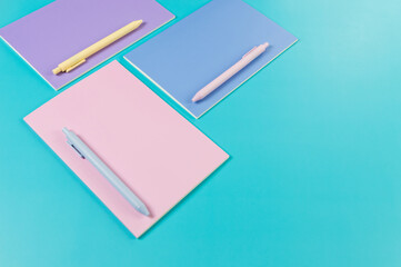 Top view of pink, purple and blue notebooks on blue background. Pink, yellow and blue pens, school, office wallpaper. Flat lay, copy space.