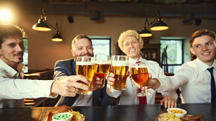 Colleagues cheerfully clink their beer glasses together at bar, enjoying after-work relaxation in laid-back atmosphere.