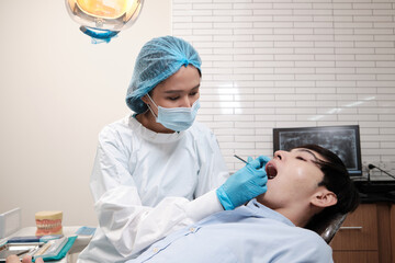 Asian female dentist examine young male patient teeth and toothache stomatology in dental clinic, well-being hygiene checks, and professional orthodontic healthcare work in doctor's office hospital.