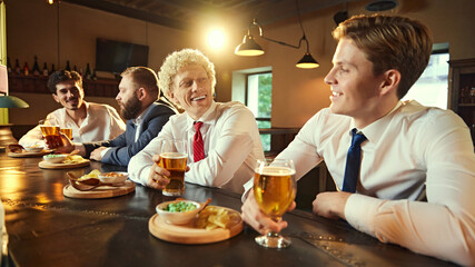 Conversations flow as group enjoys drinks and snacks. Laughter and camaraderie fill room, capturing essence of post-work bonding.