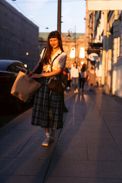 A young woman walks through the city in the golden sunset light.