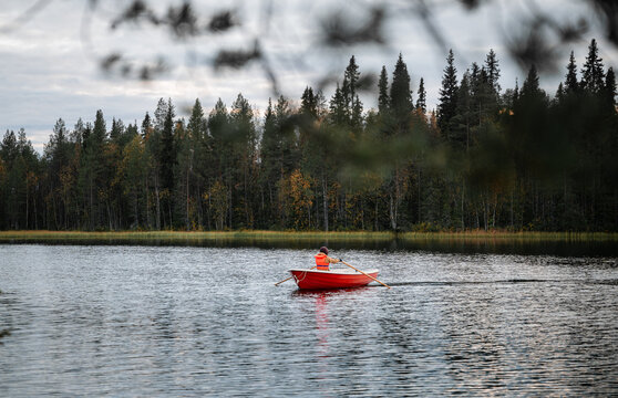 man in a life jacket rowing on a boat in autumn lake in Finland