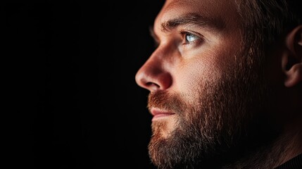 Obraz premium A man with a beard and blue eyes gazes into the distance against a black backdrop ..Or, for a more concise version: Man with