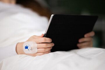 Close up shot patient in hospital bed holds tablet in hands.