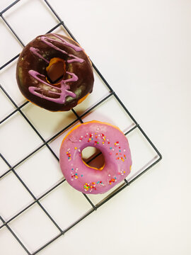 top view of two donu isolated on a white background. chocolate donuts with purple cream and purple donuts with colorful sprinkles. sweet and delicious food. Vertical photo
