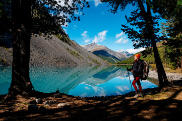Fototapeta premium a tourist girl walks with a backpack along the shore of the mountain lake Shavlinskoye in autumn