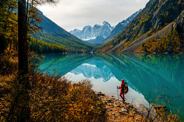 a tourist girl walks with a backpack along the shore of the mountain lake Shavlinskoye in autumn